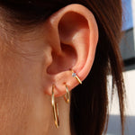 Goldene Classic Thin L Creolen am Ohr getragen, kombiniert mit kleinem Hoop und Stein-Ohrstecker.