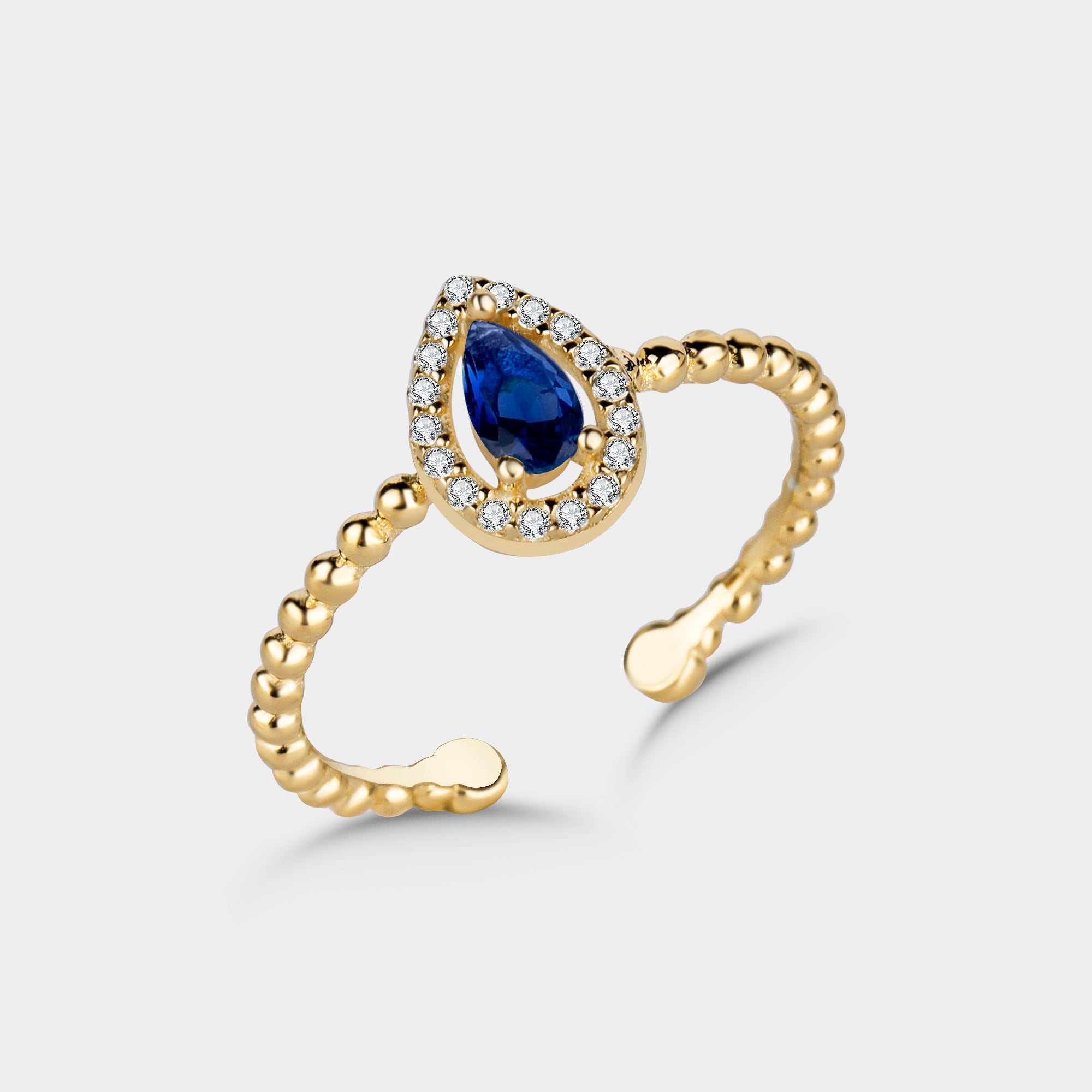Detailansicht: goldvergoldeter Ring mit blauem Saphir-Zirkonia im Tropfenschliff und funkelnden weißen Steinen.