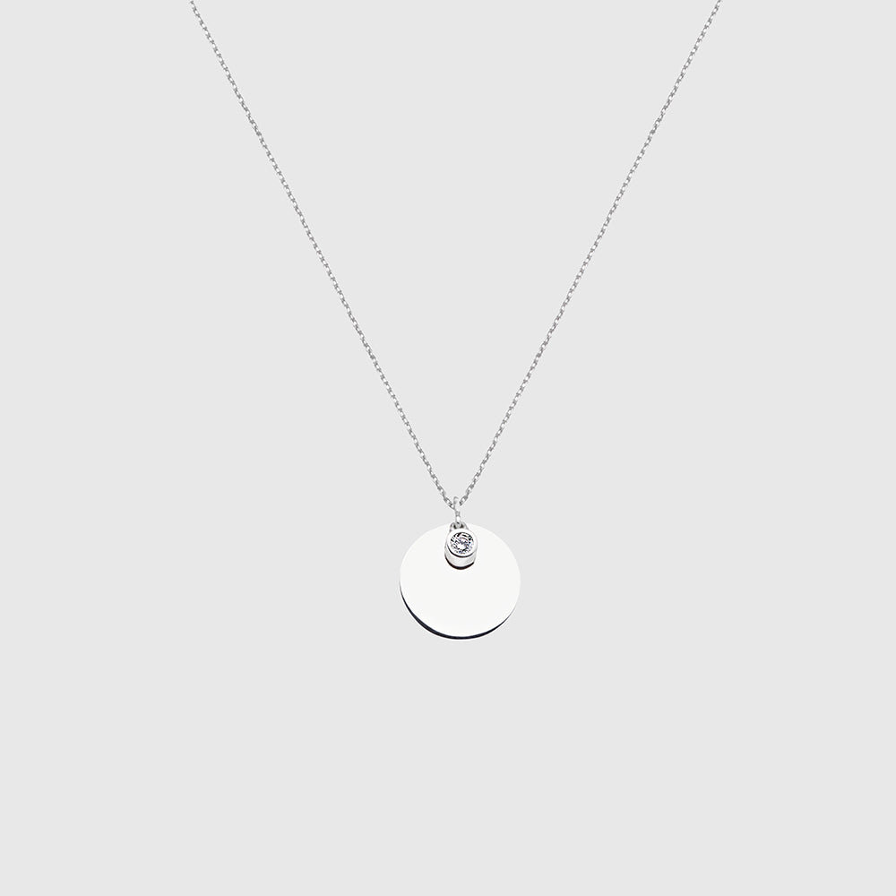 Halskette mit rundem Silberanhänger und kleinem Zirkonia-Stein vor hellem Hintergrund.