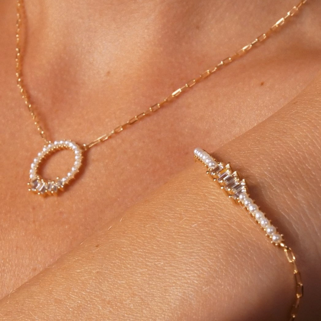 Detailaufnahme Pearl X Baguette Halskette und Armband in Gold auf der Haut.
