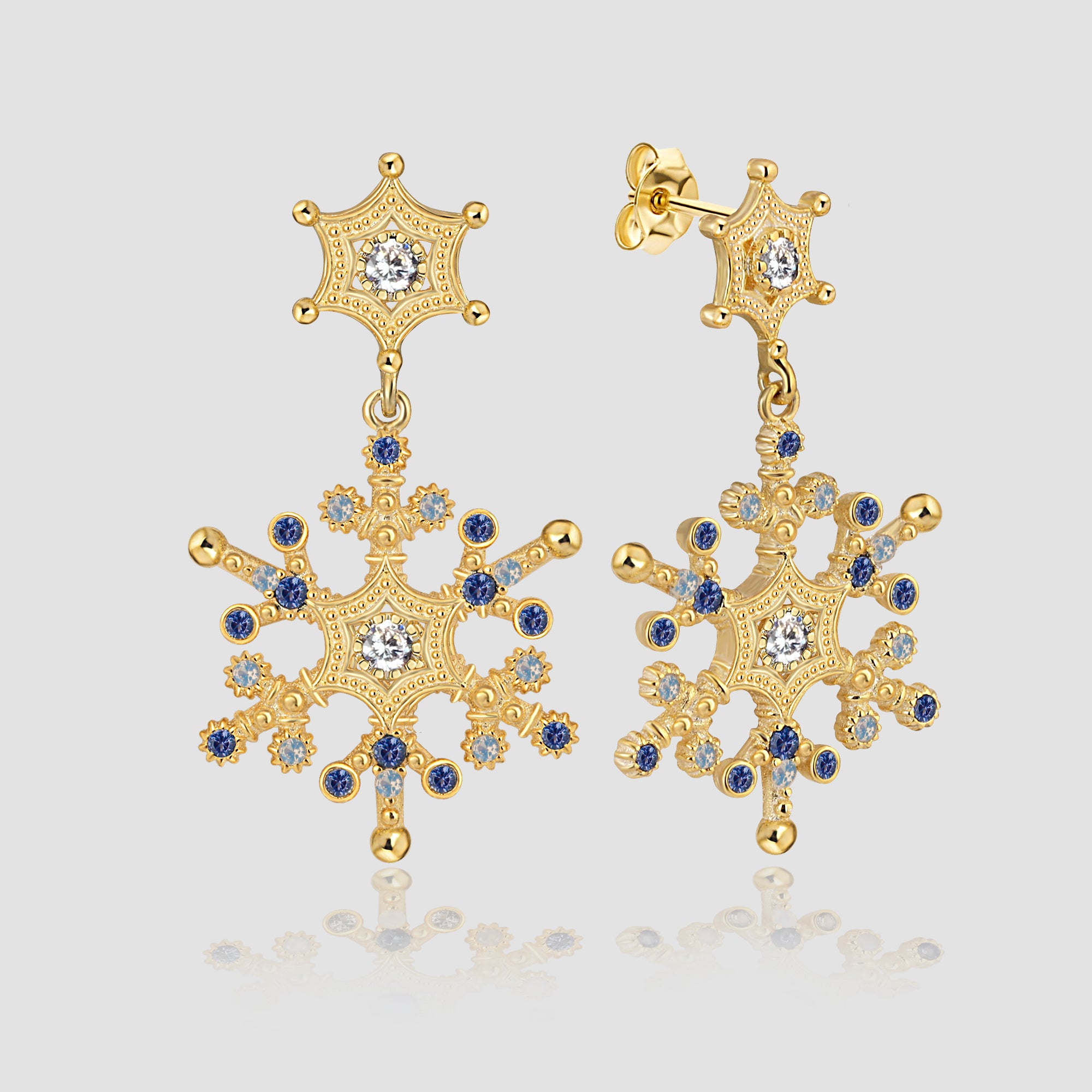Snowflake Ice X Ohrringe Gold – Schneeflocken Anhänger mit blau-weißem Zirkonia Mix auf grauem Hintergrund.