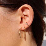 Goldener Solitär Ear Cuff mit Zirkonia am Ohr getragen, kombiniert mit Creolen.