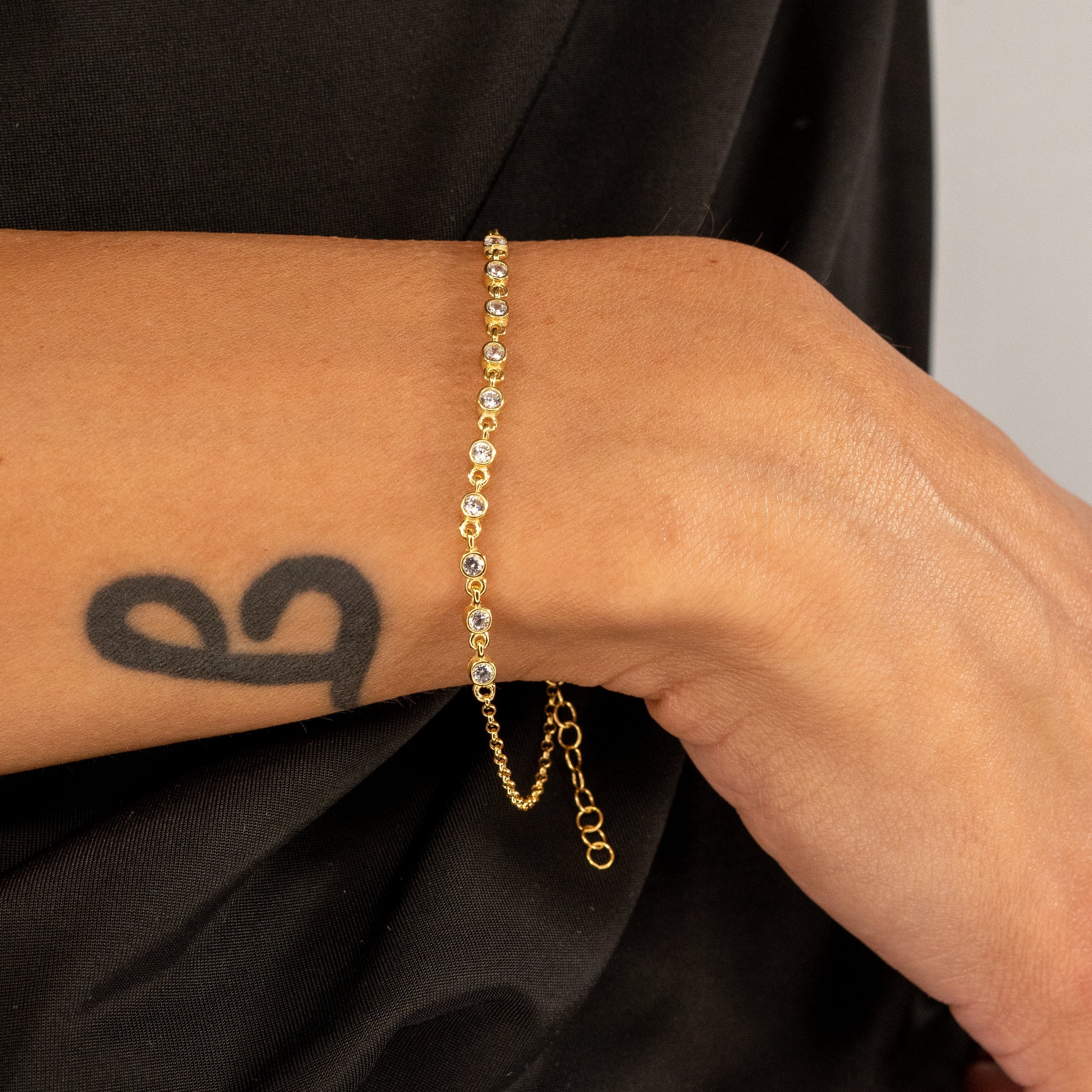 Sparkle Zirkonia Goldarmband am Handgelenk einer Frau mit Tattoo.