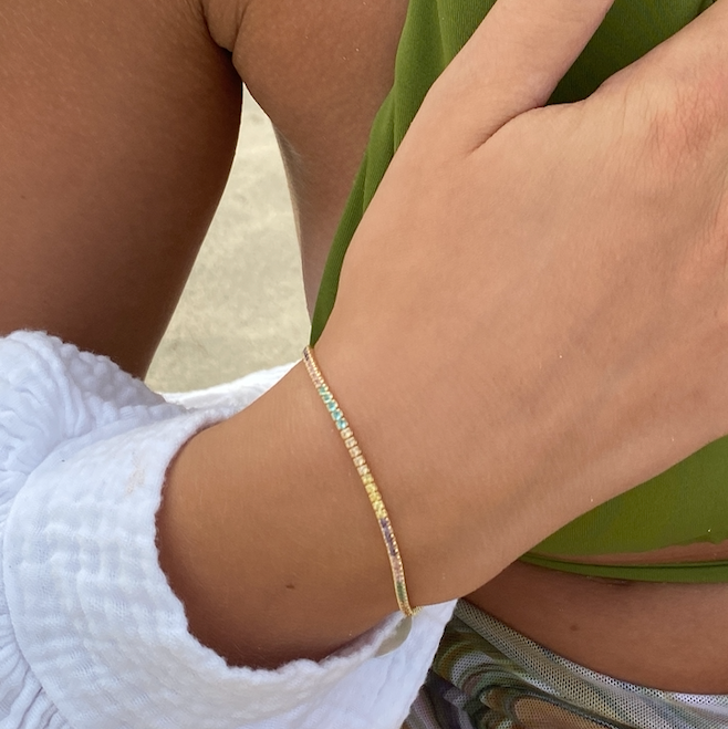 Goldene Tennis Armkette Mini Bunt mit bunten Zirkonia am Handgelenk einer Frau mit grünem Outfit.