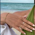 Goldene Tennis Armkette Mini Bunt am Handgelenk einer Frau am Strand, kombiniert mit Ringen.